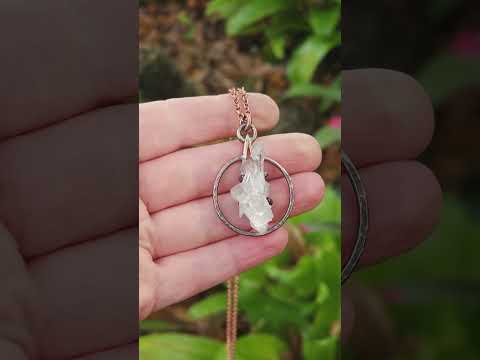Arkansas quartz cluster necklace held in hand against natural background.