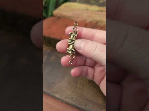 Woven brass loc bead held in hand against a wood and brick background.