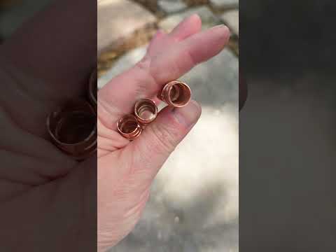 Set of 3 copper hair beads held in hand against stone background.