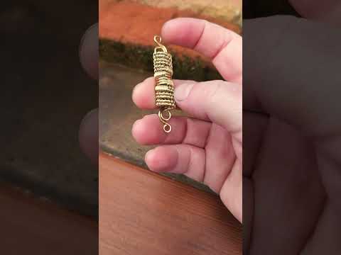 Woven brass dreadlock bead held in hand against wood and brick background.