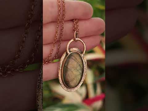 Copper and labradorite pendant held in hand to show stone color flash.
