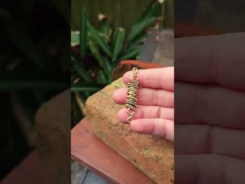Woven brass hair bead held in hand against brick and wood background.