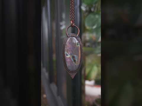 Copper pendant with a colorful stone on a blurred outdoor background