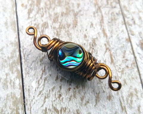 Abalone dread bead on a white wood background.