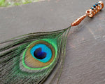 Peacock eye feather dread bead on a wood background.