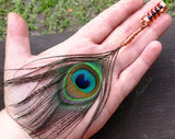Peacock eye feather dread bead in a hand to show scale.