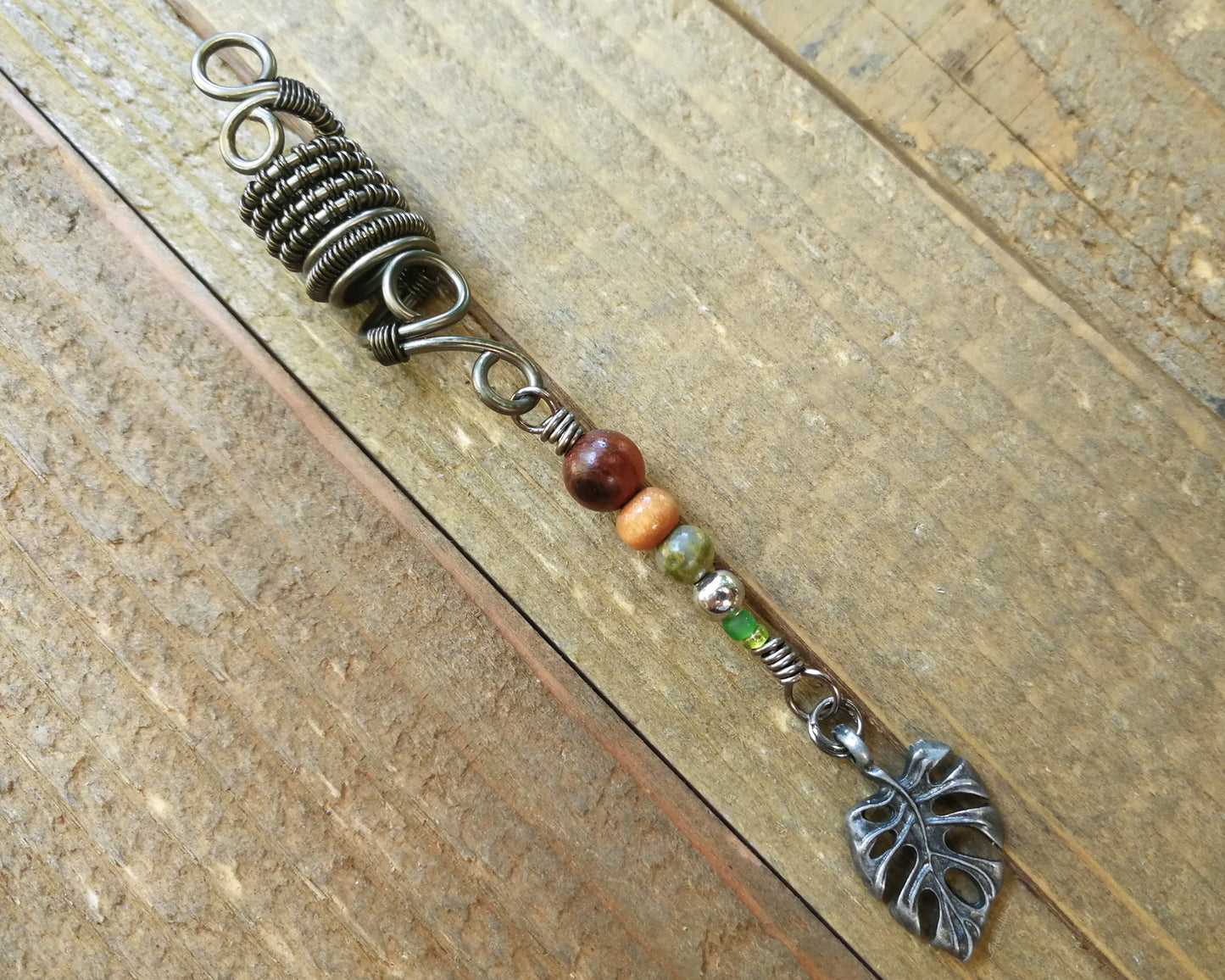 A close up view of a Hematite Leaf Dread Bead on a wooden background.
