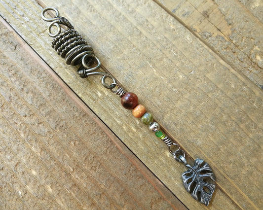 A close up view of a Hematite Leaf Dread Bead on a wooden background.