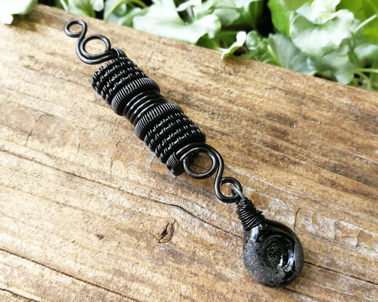 Black stardust glass dread bead on a wood backdrop.
