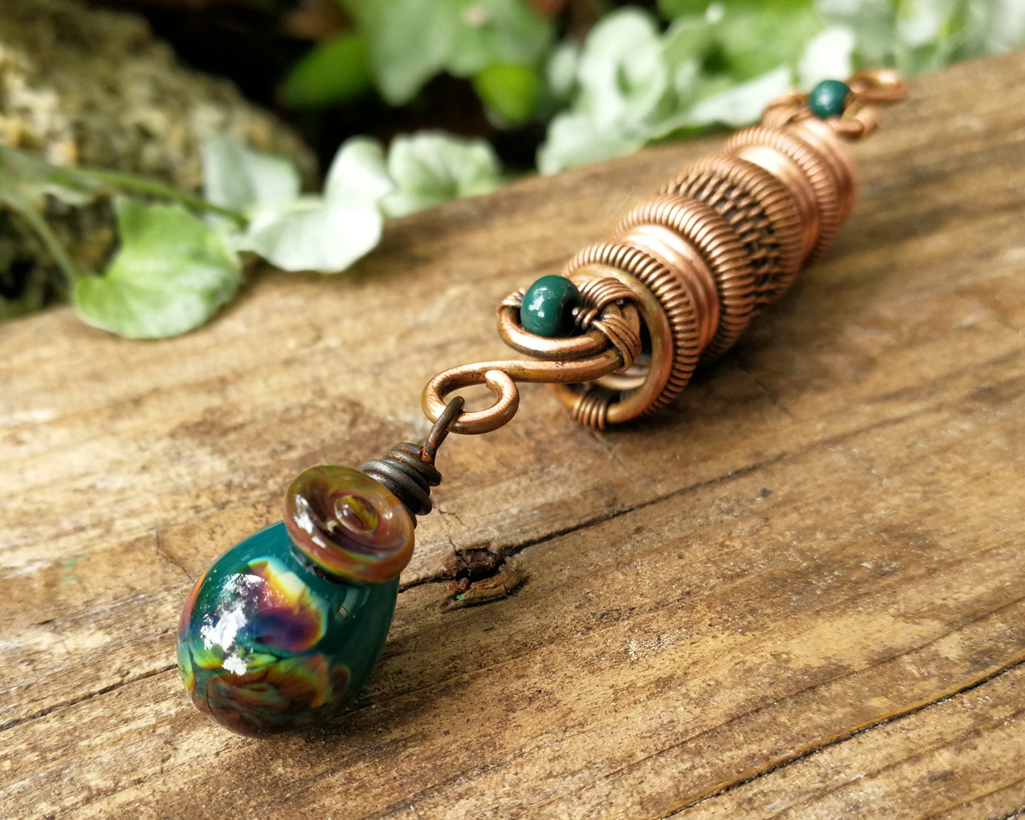 Woven copper dreadlock bead with turquoise glass on a wood background.