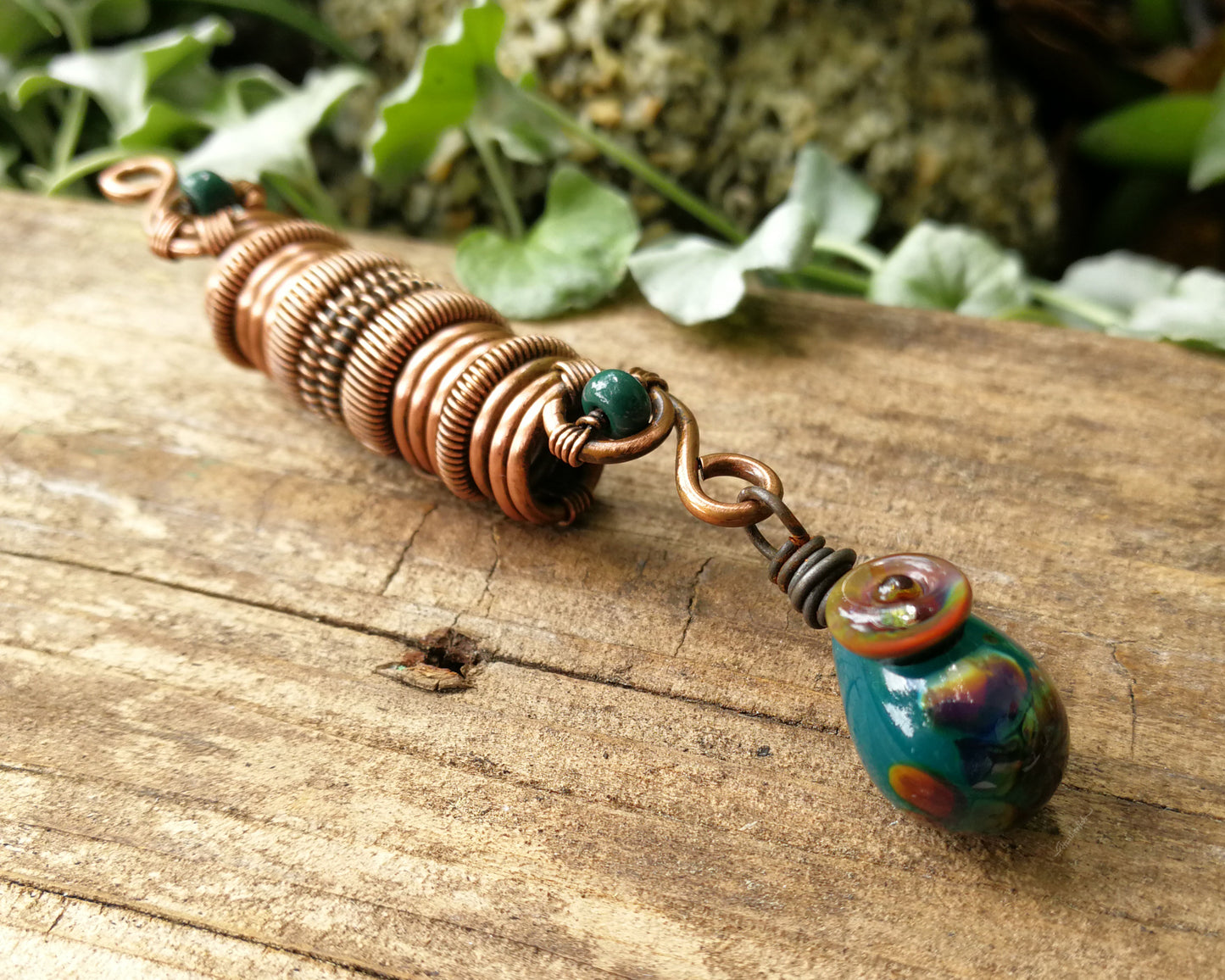 Woven copper dreadlock bead with turquoise glass on a wood background.