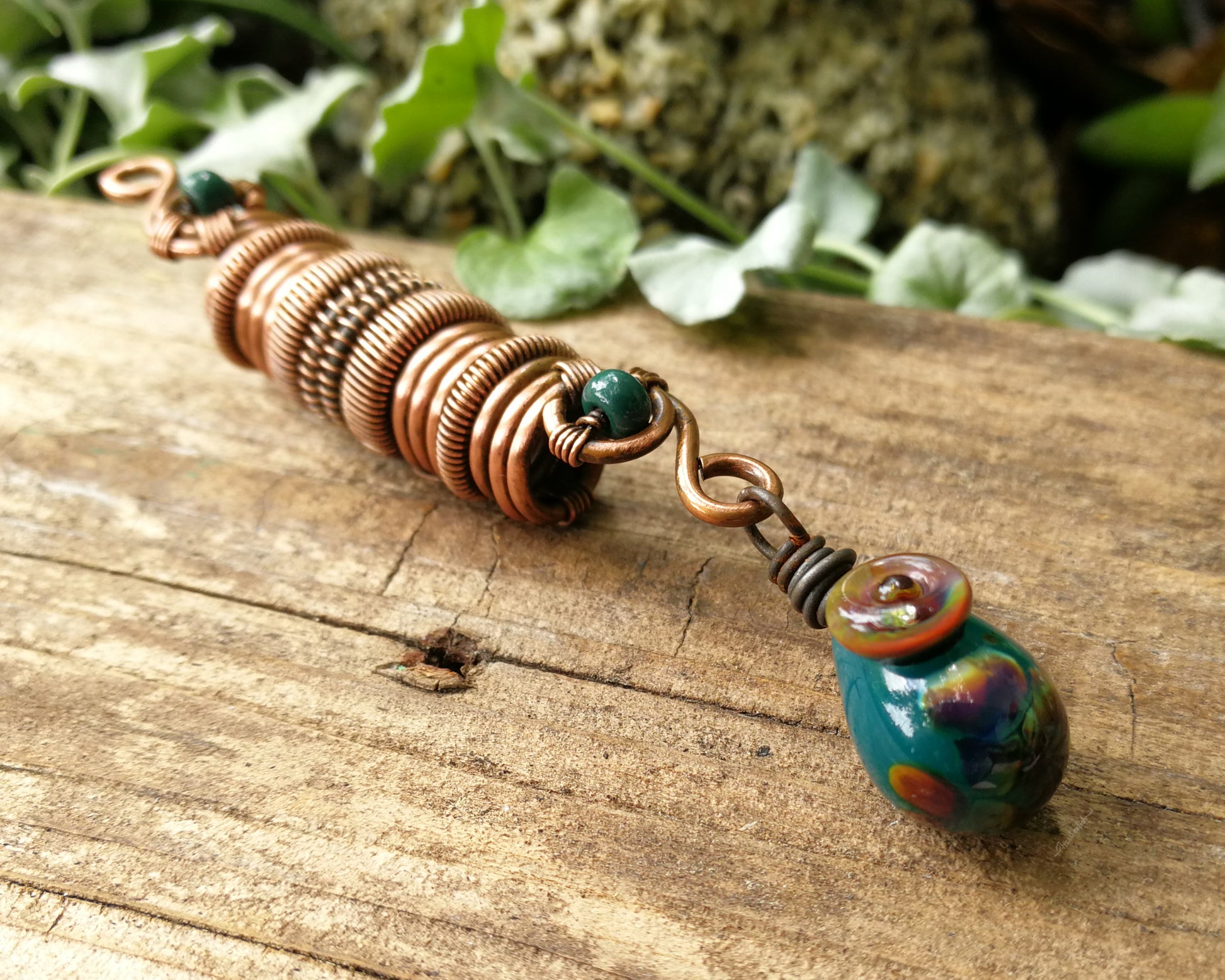 Woven copper dreadlock bead with turquoise glass on a wood background.