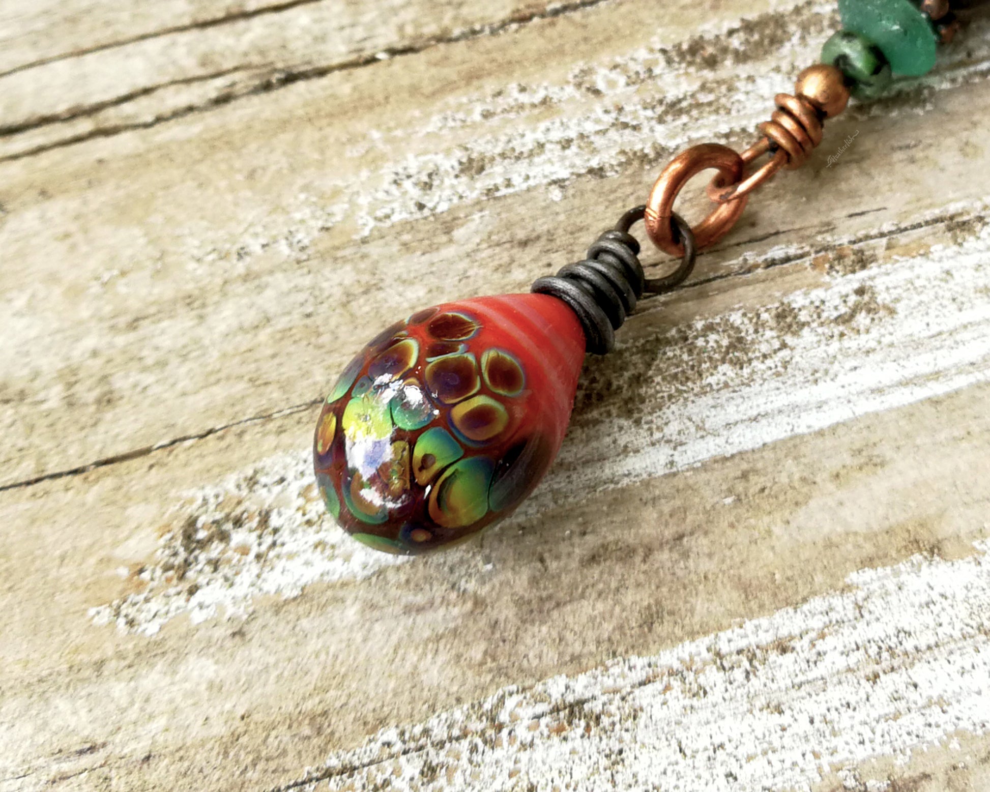 Woven copper dreadlock bead with coral colored artisan glass on a wood background.