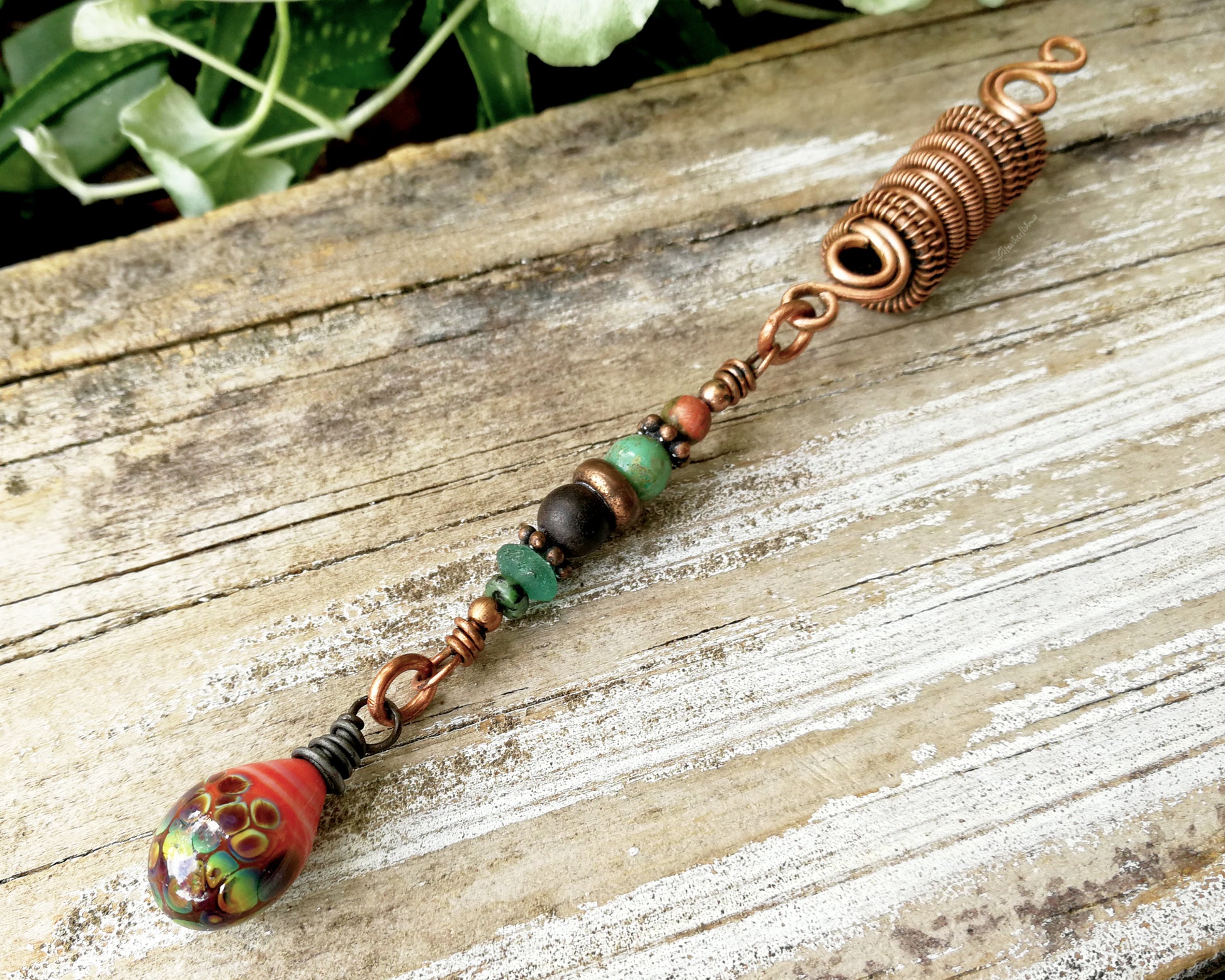 Woven copper dreadlock bead with coral colored artisan glass on a wood background.