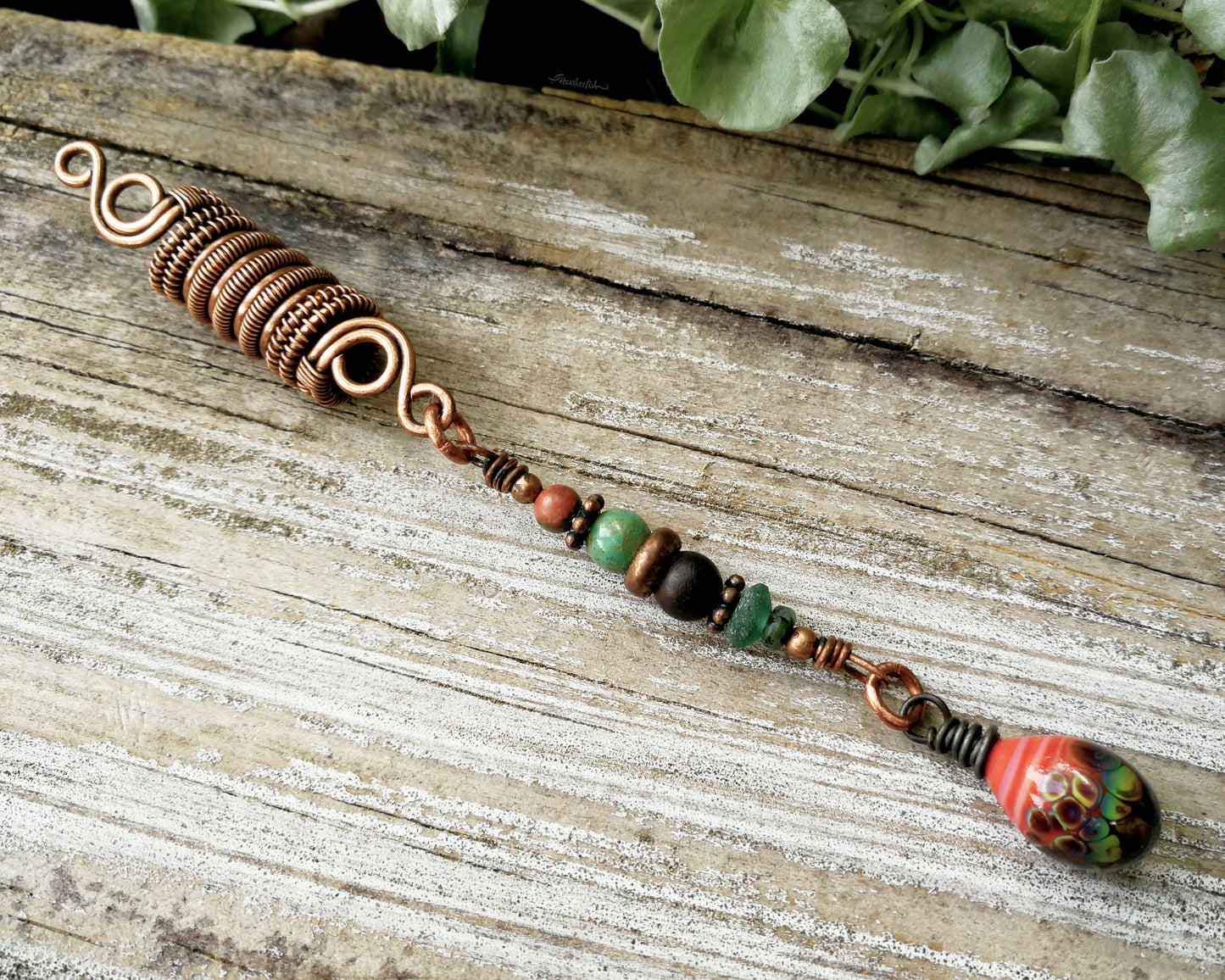 Woven copper dreadlock bead with coral colored artisan glass on a wood background.