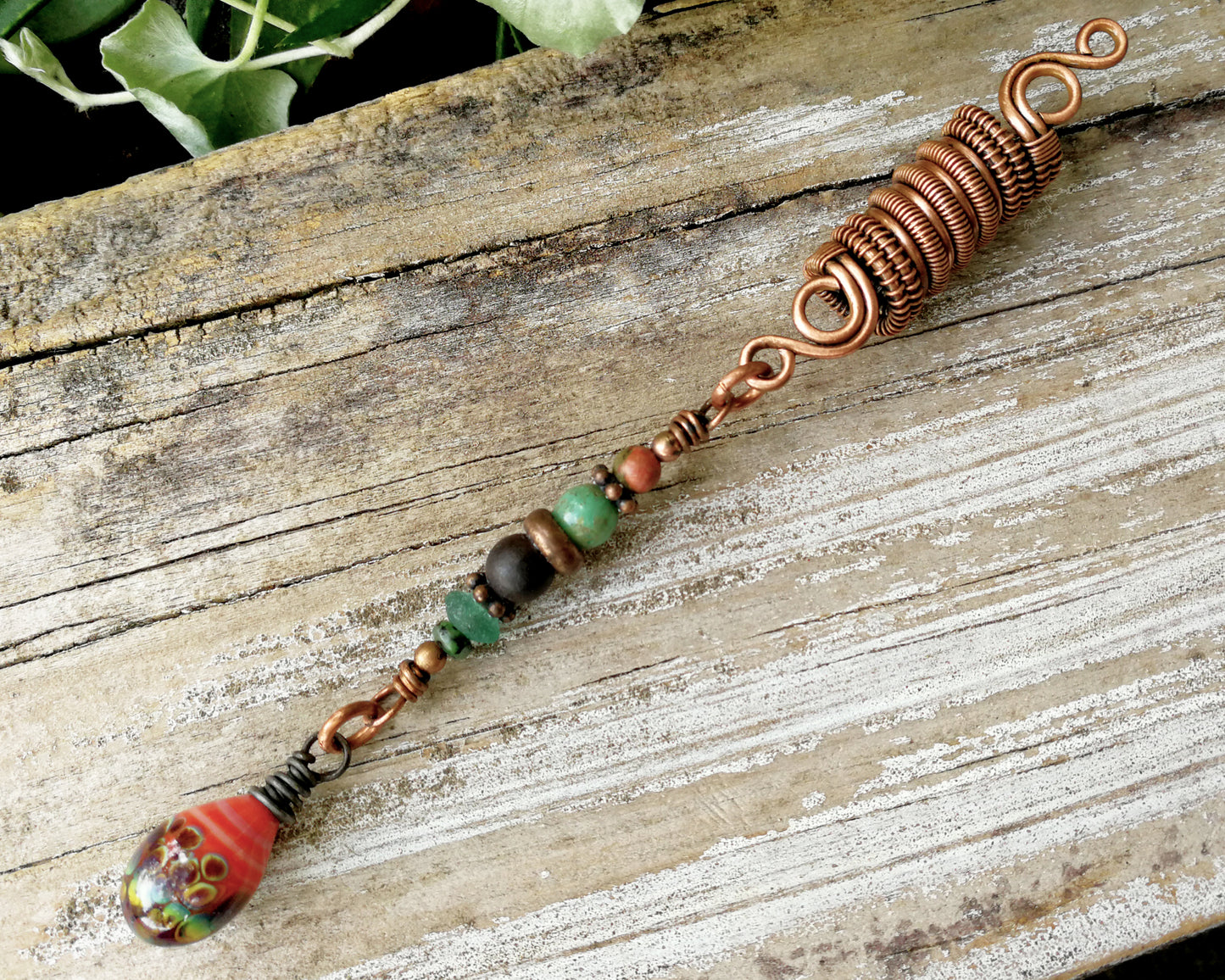Woven copper dreadlock bead with coral colored artisan glass on a wood background.