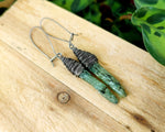 Green kyanite earrings wrapped with fine silver filled wire. Shown against wood background.