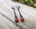 Red Jasper Earrings with black findings on a wood background.