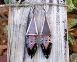 Obsidian Arrowhead Copper Earrings on a wood background.