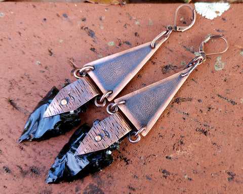 Obsidian Arrowhead Copper Earrings on a brick background.