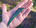 A peacock feather blade dread bead in a hand for size reference.