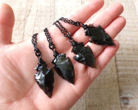 Black obsidian arrowhead necklace held in hand to show scale.