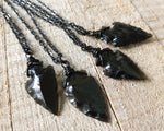 Black obsidian arrowhead necklace shown on wood background.