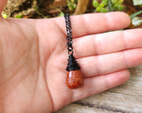 Fire agate necklace on a black chain, held in hand to show scale.