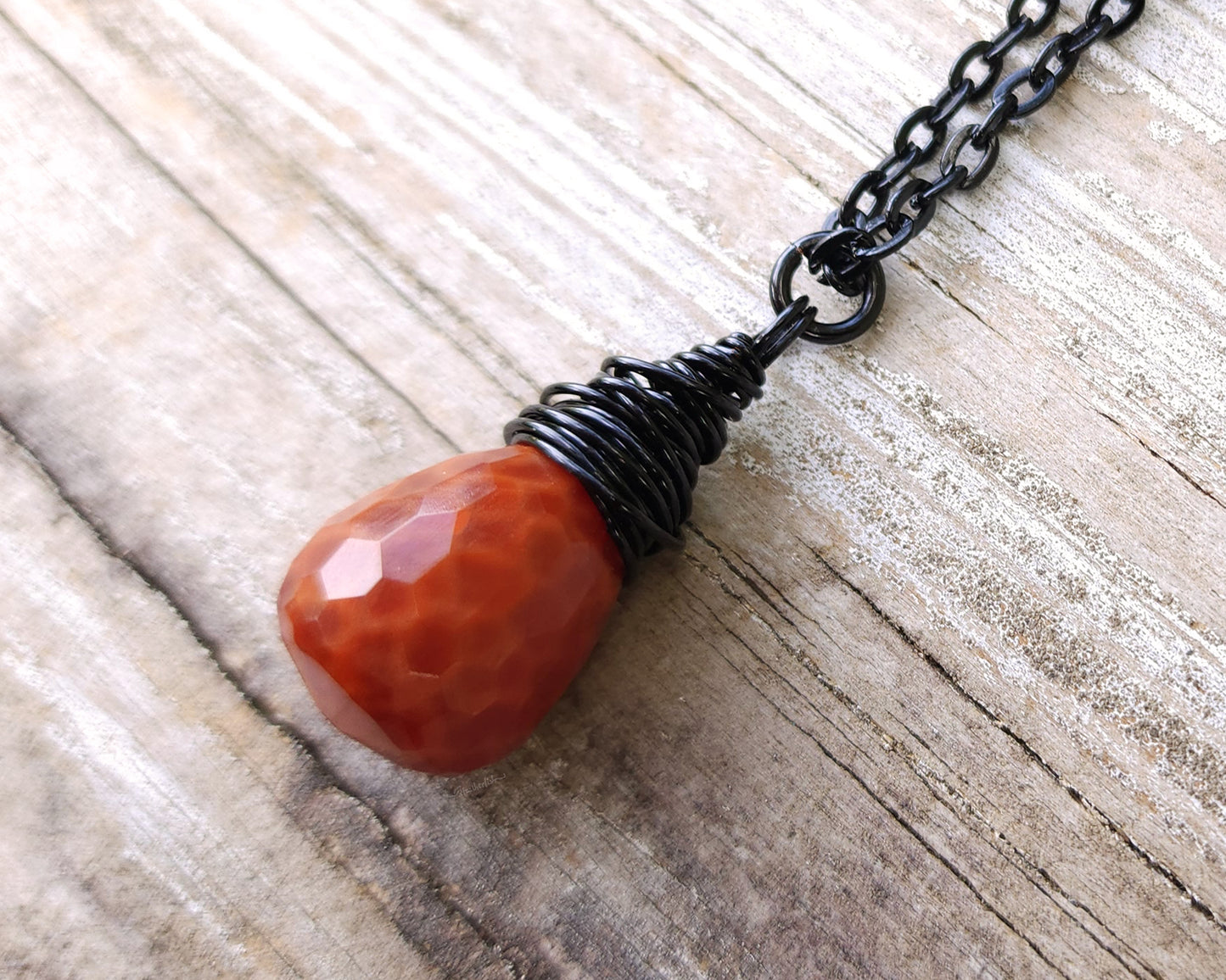 Fire agate necklace on a black chain on wood background.