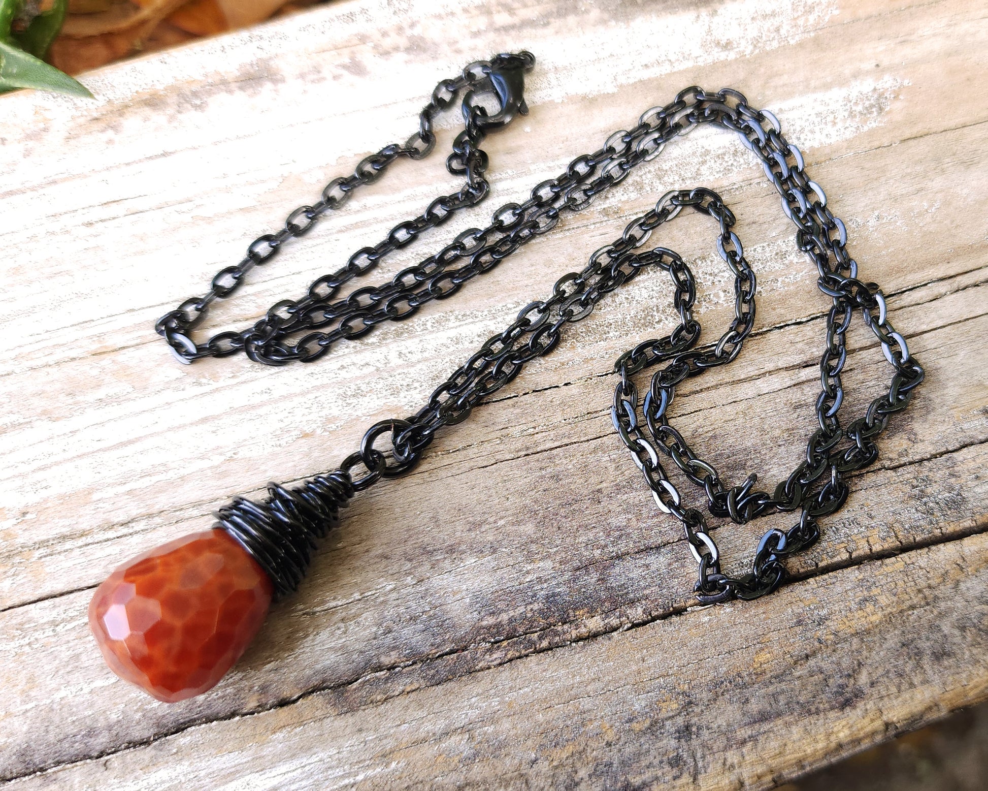 Fire agate necklace on a black chain on wood background.