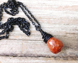 Fire agate necklace on a black chain on wood background.