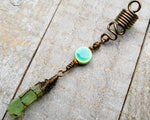 A close up view of a Green Kyanite Squiggle Loc Bead on a wooden background. 