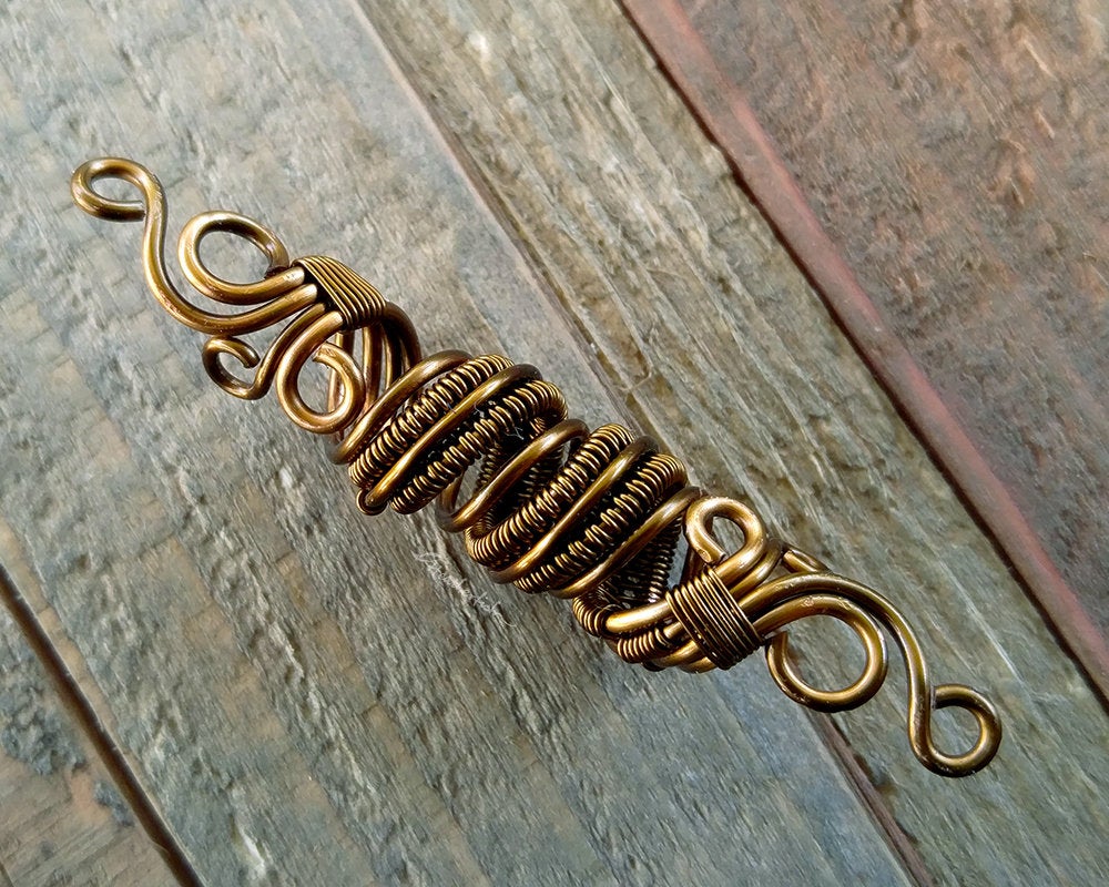 A top view of a Fancy Woven Filigree Dread Bead on a wooden background. 