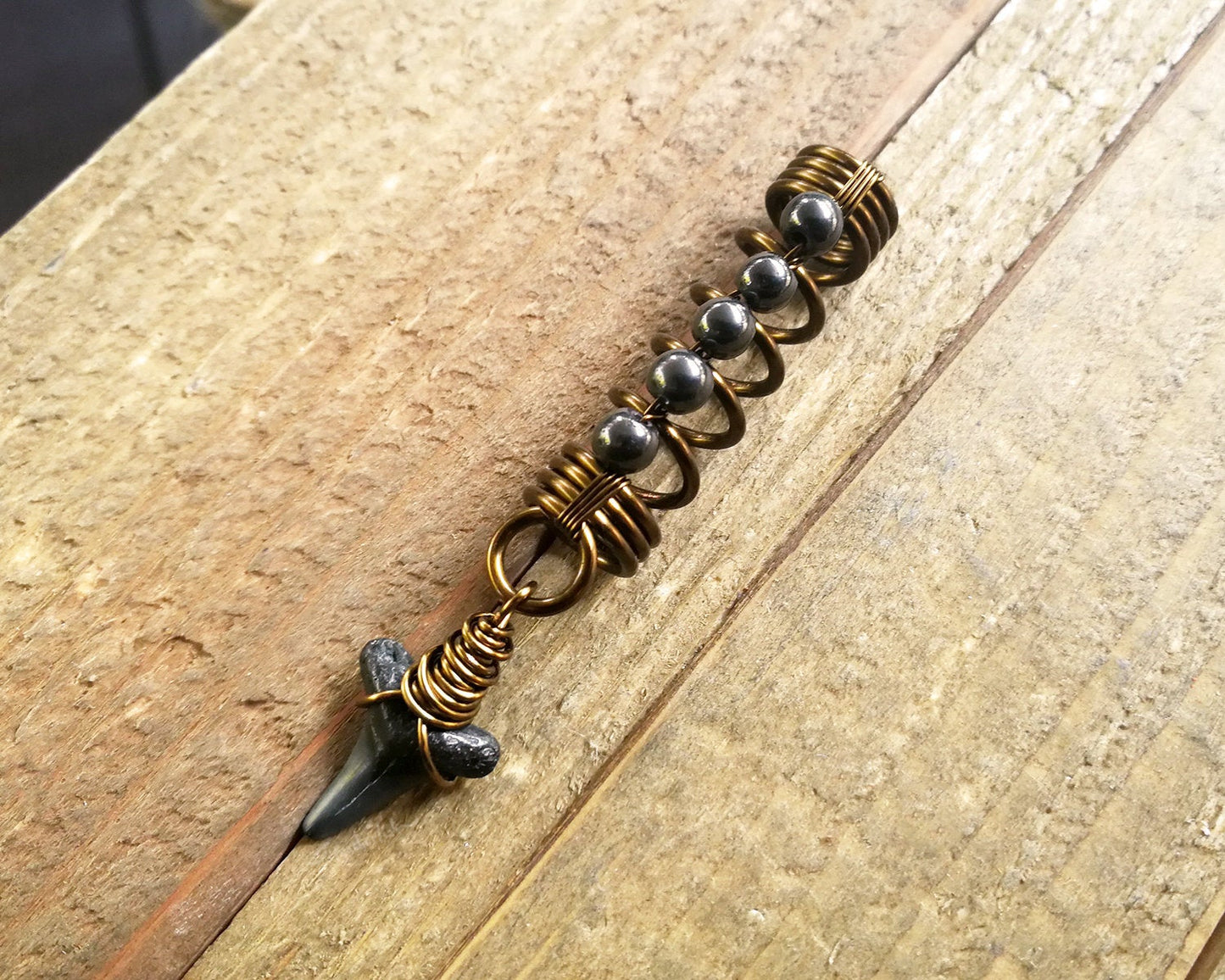 A top view of a Shark Tooth Dread Bead with Hematite Accents.