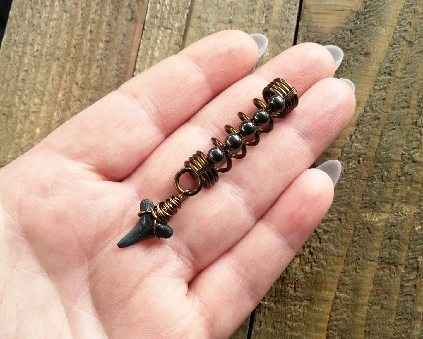 A top view of a Shark Tooth Dread Bead with Hematite Accents in hand.