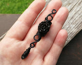 A top view of a Goth Dreadlock jewelry Black Rose in hand.
