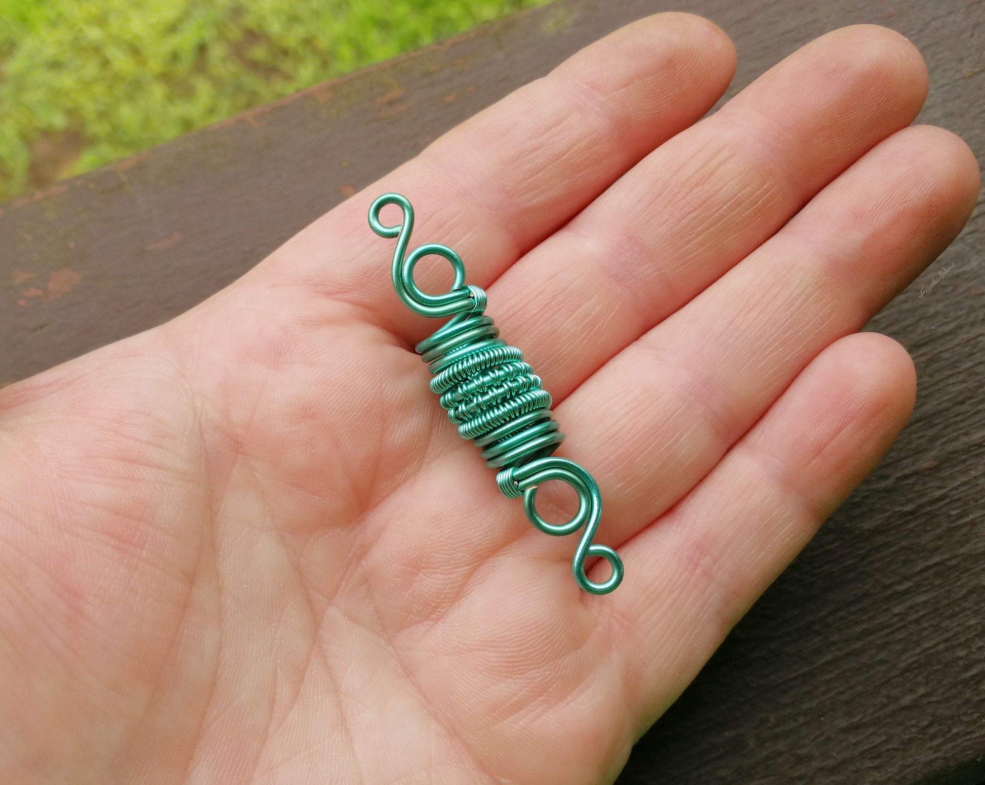 A top view of a Woven Aqua Dread Bead in hand.