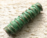 A close up view of a Green Patina Copper Dread Bead. 